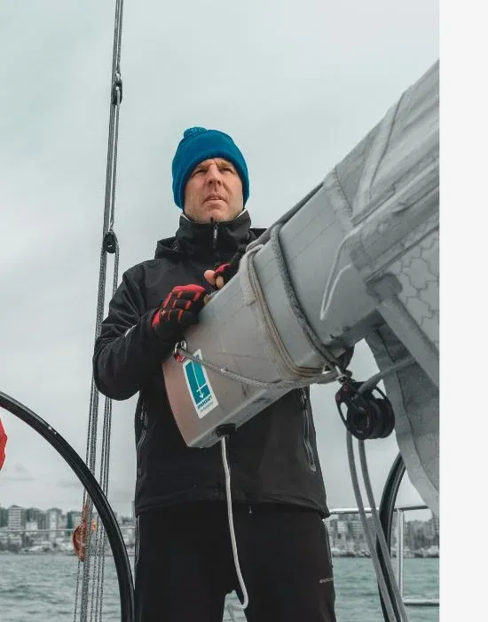 Skipper au bonnet bleu réglant une voile par temps gris